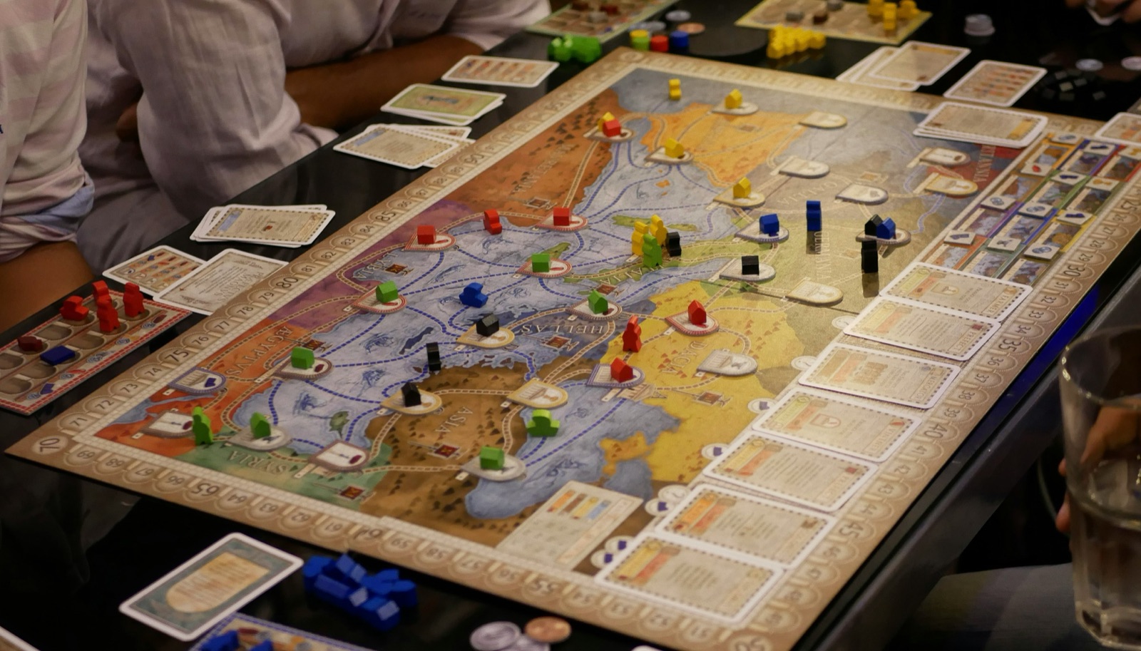 Players around a board game mid-session with cards and tokens on the table
