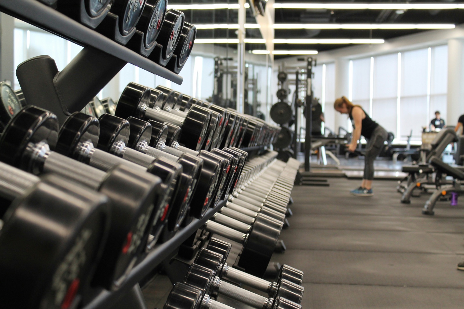 Rack of dumbbells on the gym floor with a member training in the background
